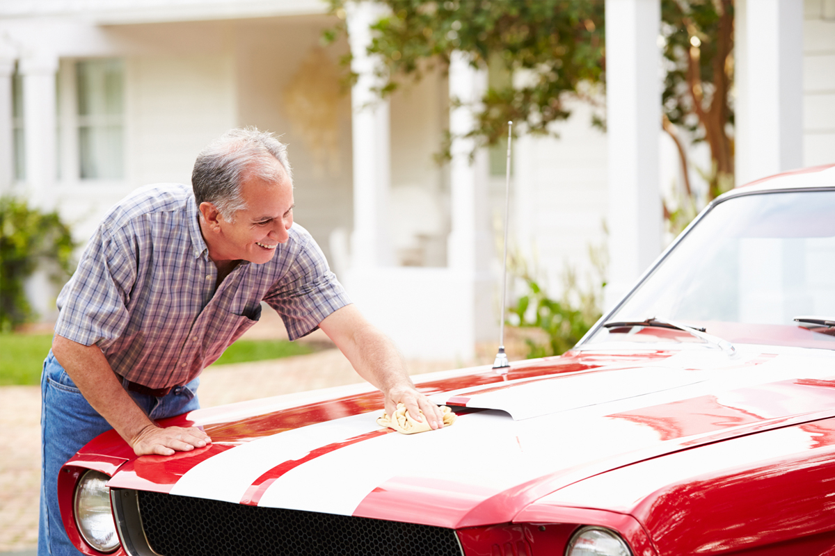 Hombre mayor pasando la mano por el cofre de un Mustang rojo.