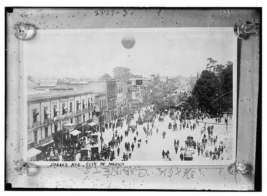 Vista elevada de la avenida Juárez llena de gente, carruajes y automóviles.