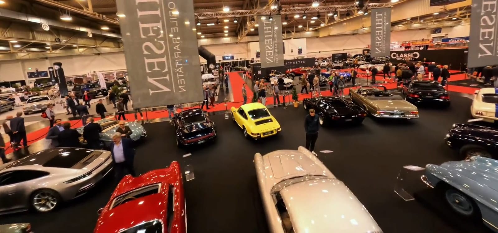 Pabellón de la Techno Classica Salon con decenas de autos clásicos y visitantes bajo grandes estandartes.