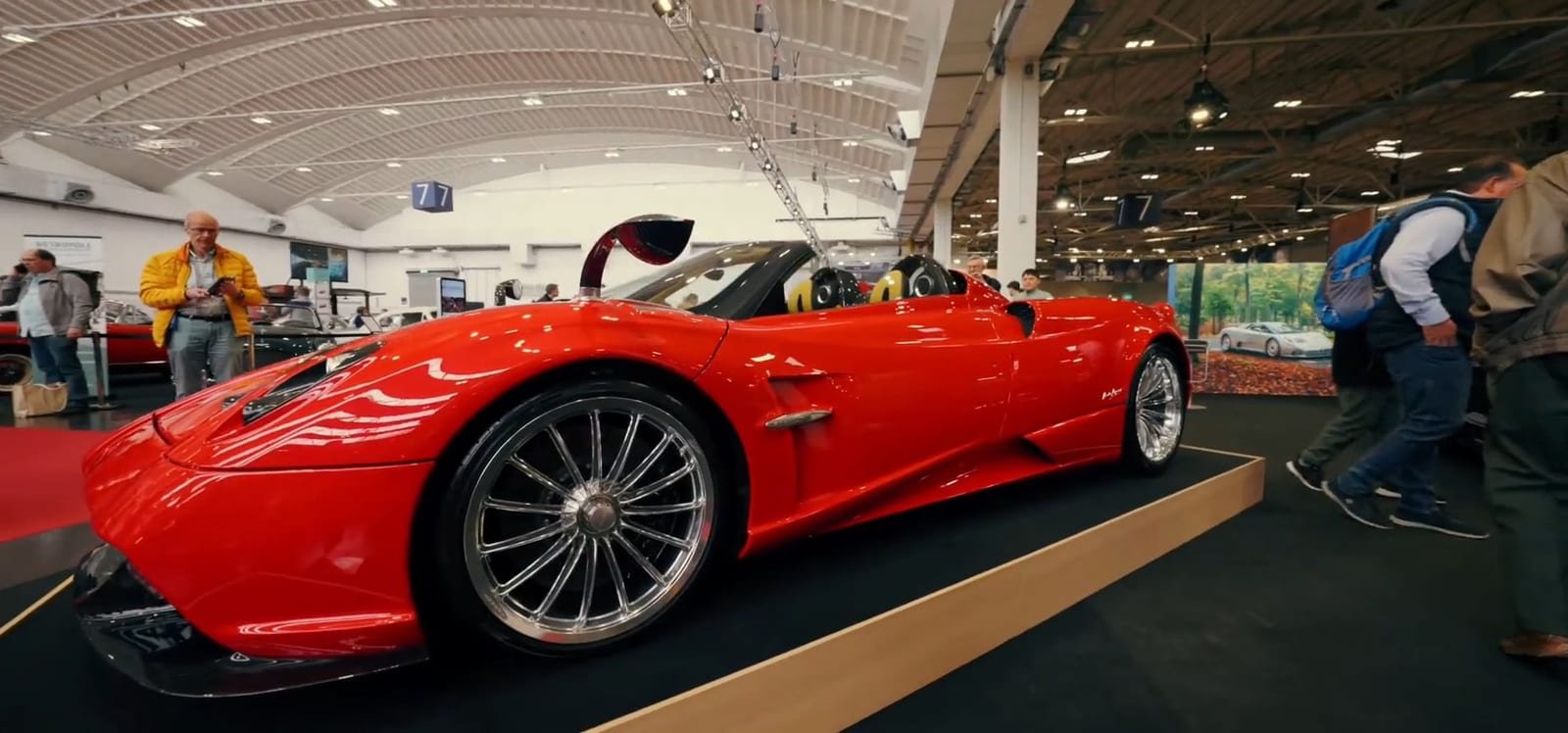 Pagani rojo descapotable exhibido sobre una plataforma, rodeado de visitantes.