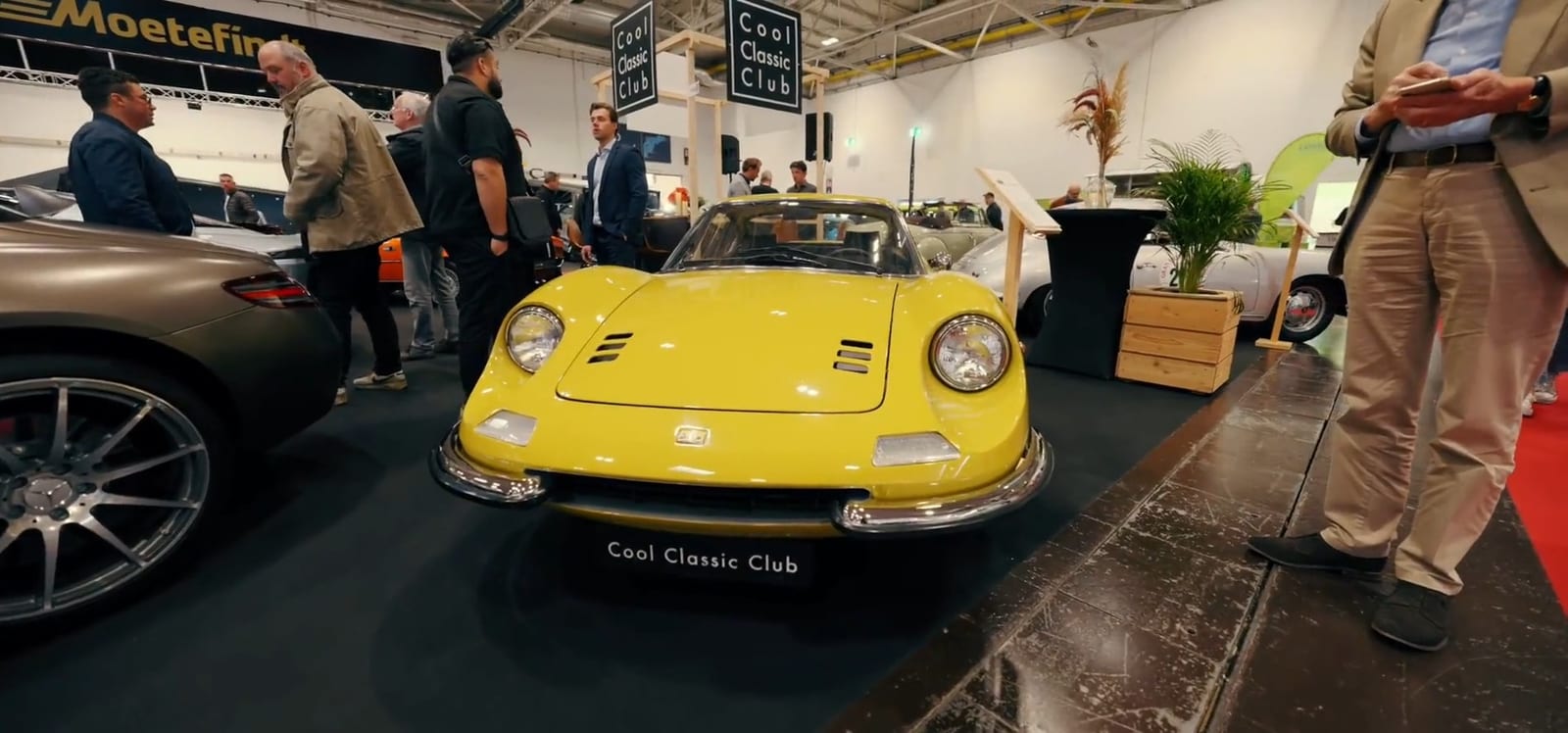 Ferrari Dino amarillo en el módulo de un club, con visitantes conversando.